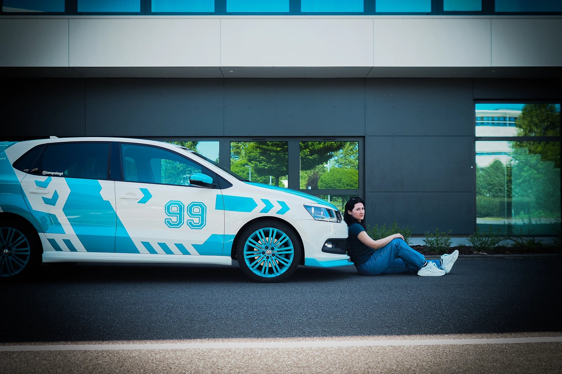 Person sitting next to a futuristic car with blue and white design in an urban setting
